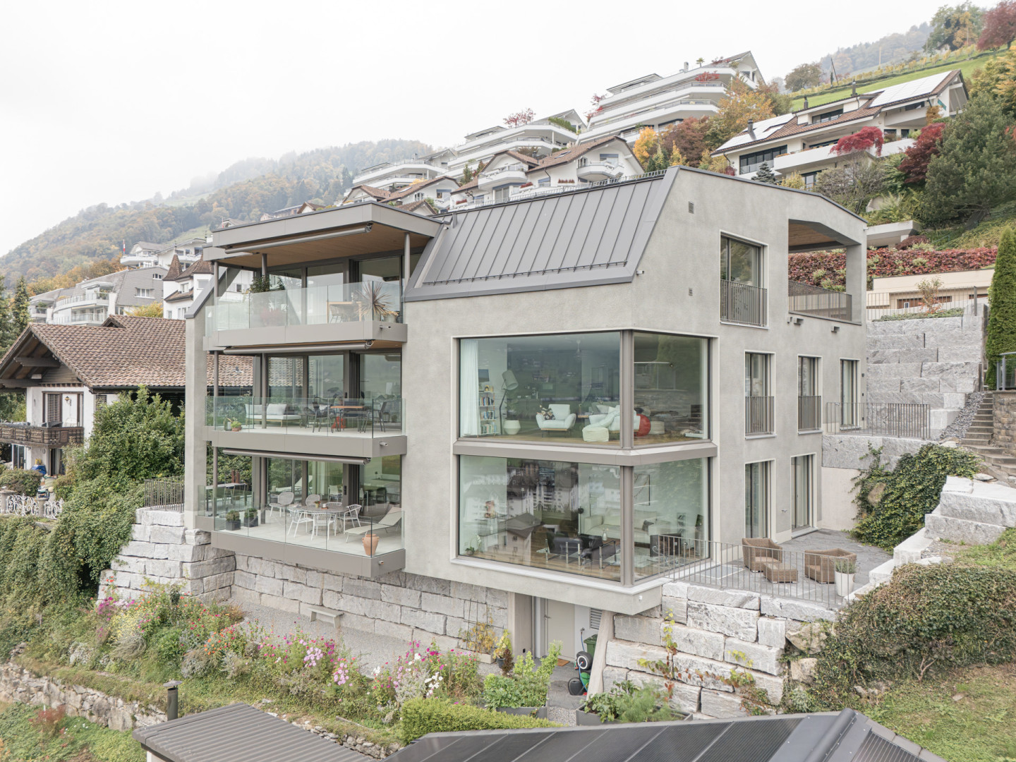 Drohnenaufnahme der Frontfassade mit auskragenden Balkonen und Panoramaverglasung, eingebettet ins Hangquartier